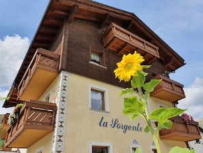 A multi-story building with balconies, a prominent sunflower, and the name 'La Sorgente' on the facade.