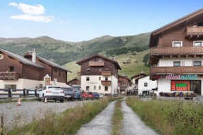 A rural mountain village with wooden buildings, a road, and parked cars.