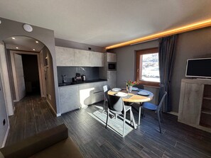 Una cocina compacta con electrodomésticos modernos, un comedor con mesa y sillas, y un televisor sobre un mueble de madera.