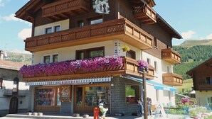 Un edificio de madera de varios pisos, con balcones, una tienda en la planta baja y montañas al fondo.
