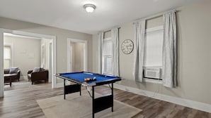 Une pièce avec une table de billard, une horloge au mur et une fenêtre avec des rideaux.