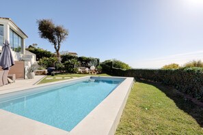 A rectangular swimming pool with a tiled edge, surrounded by a well-maintained lawn and a hedge.