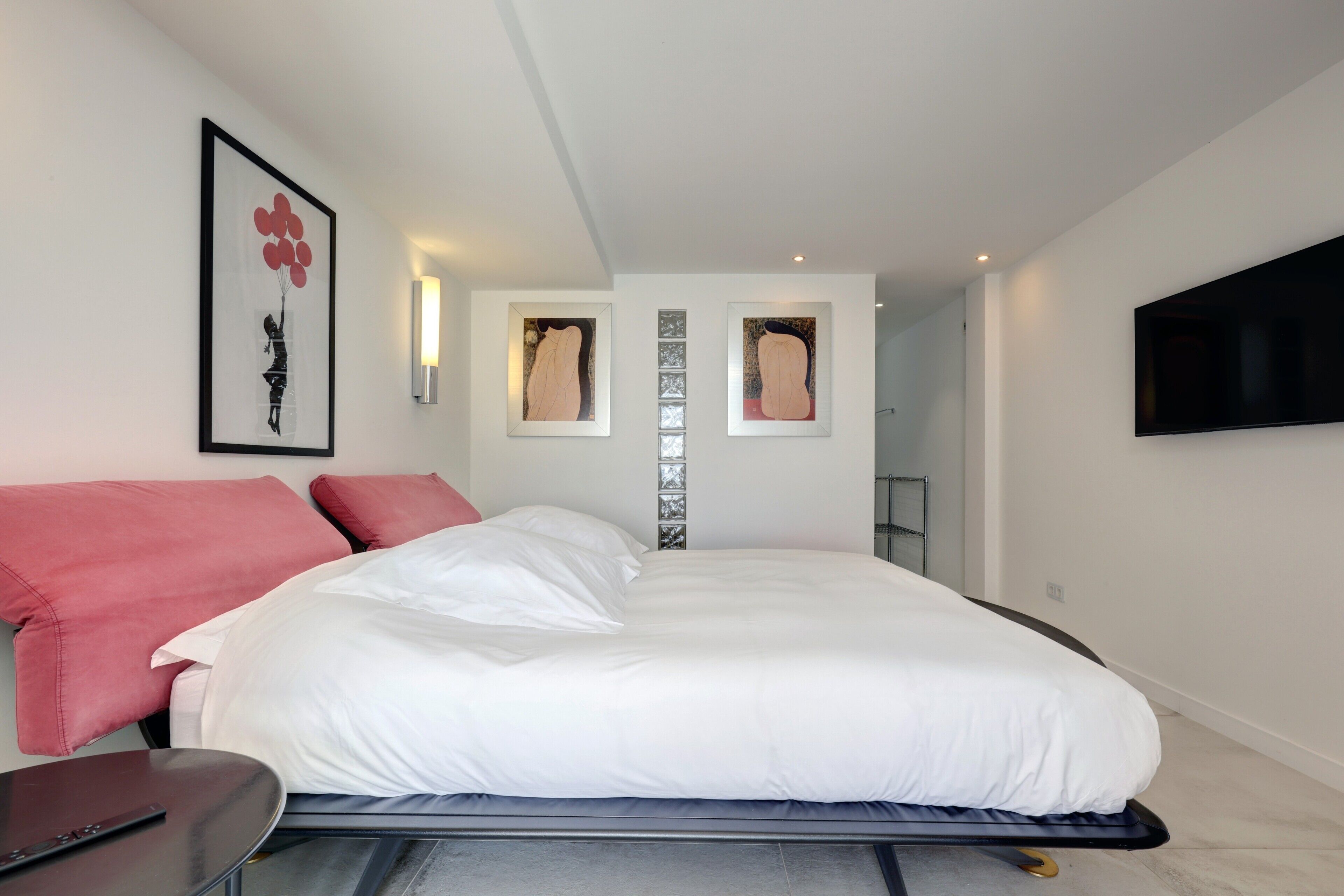 Un dormitorio moderno con una cama grande, un televisor montado en la pared y obras de arte enmarcadas sobre la cama.