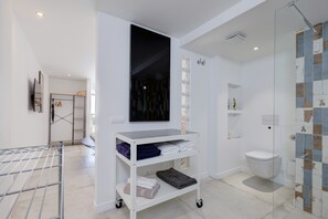 A modern bathroom with a glass shower enclosure, a white sink, and a wall-mounted shelf with towels.