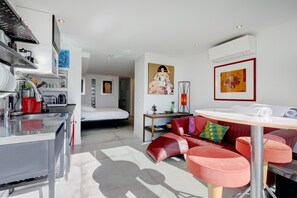 A modern hotel room with a kitchenette, a sofa with cushions, a bed, and artwork on the walls.