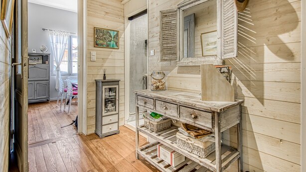 A room with wooden walls, a vintage-style mirror, a rustic wooden cabinet, and a dining area with a table and chairs.