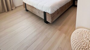 Un dormitorio con cama, ventana con cortinas, aire acondicionado, espejo redondo y suelo de madera.