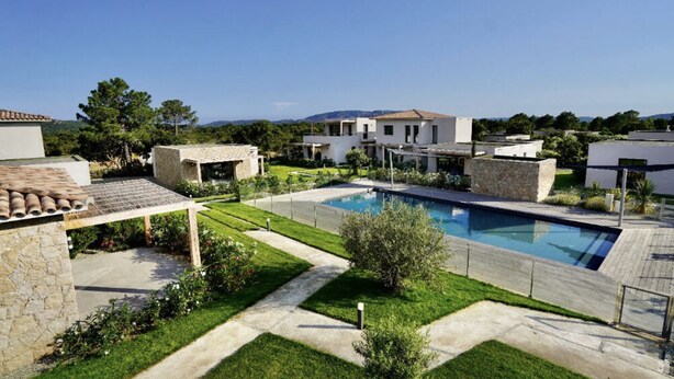 Una villa moderna con piscina, estructuras de piedra y un jardín bien cuidado.