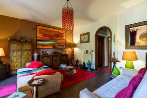 Un salon chaleureux avec un canapé, une table basse, un tapis rouge, un luminaire suspendu et un tableau au mur.