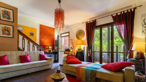 A living room with a sofa, a daybed, a coffee table with a vase, and a view through large windows.