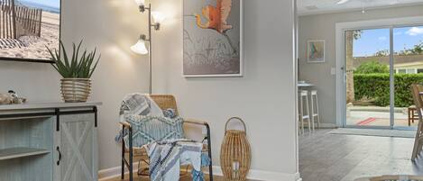 A spacious living area with a large flat-screen TV, a comfortable chair, a dining table, and a ceiling fan.
