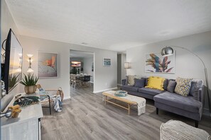 Un salon moderne avec un canapé gris, une table basse en bois et, au fond, un coin repas.