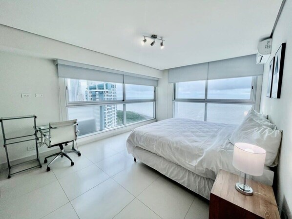 Une chambre d’hôtel moderne dotée d’un grand lit, d’un bureau avec une chaise et offrant une vue sur la ville grâce à de grandes fenêtres.