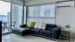 A modern living room with a black leather sectional sofa, a small side table, and a potted plant.
