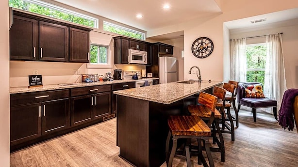 Una cocina moderna con armarios oscuros, una isla central y un comedor con sillas y mesa de madera.