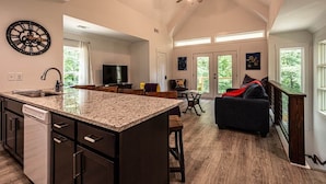 Una cocina amplia con una isla central, un área de comedor con mesa y sillas, un sofá de color oscuro y un ventilador de techo.