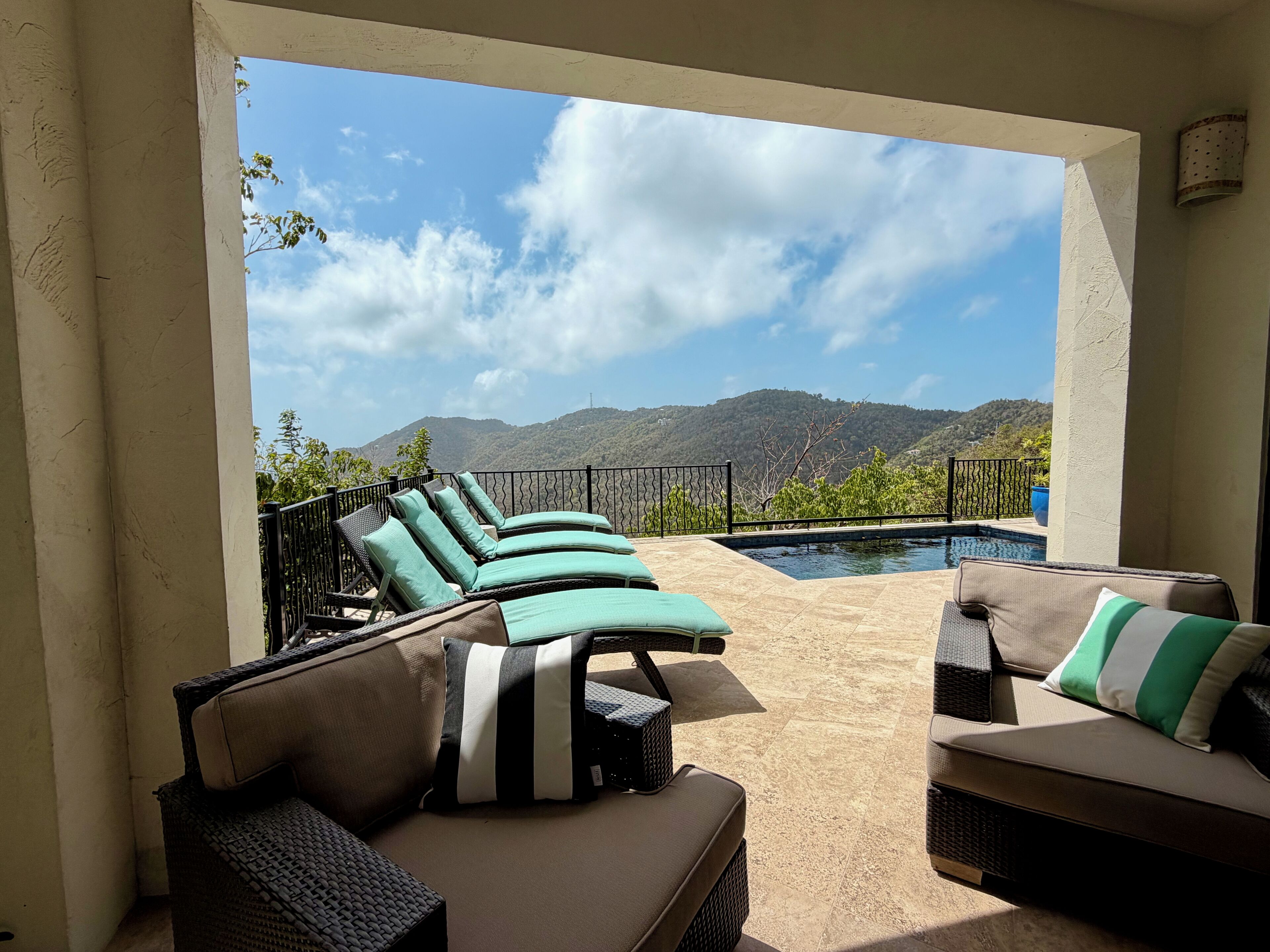 A sunlit outdoor seating area with lounge chairs and a pool, overlooking a mountainous landscape.