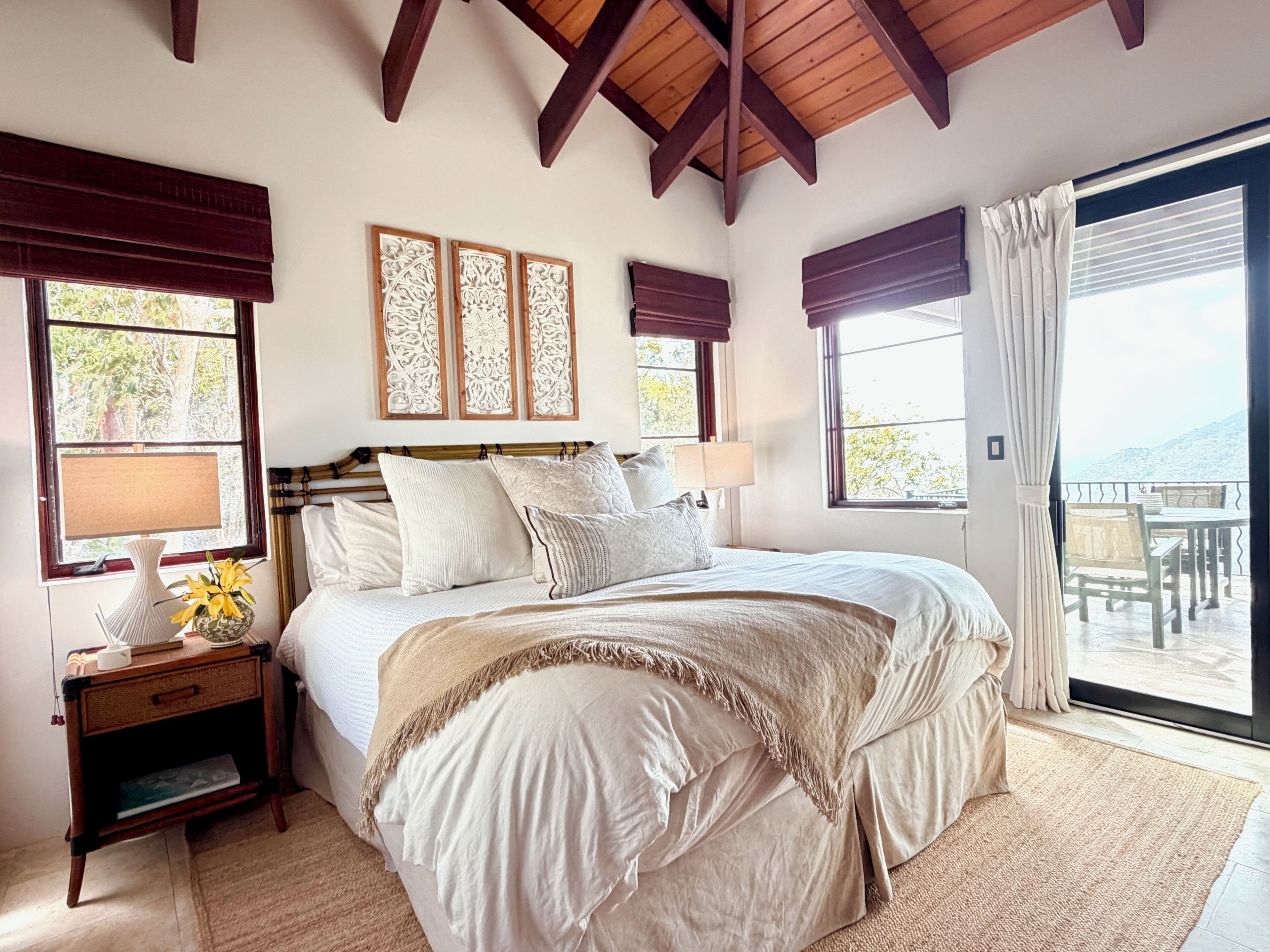A bedroom with a large bed, a nightstand, a lamp, and a view of the outdoors through a sliding door.
