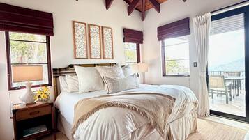 A bedroom with a large bed, a nightstand, a lamp, and a view of the outdoors through a sliding door.