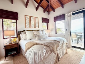 Quarto com uma cama grande, mesa de cabeceira, abajur e vista para o exterior através de uma porta deslizante.