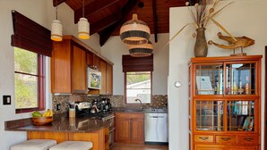 A kitchen with wooden cabinets, a central island with stools, hanging pendant lights, and a built-in bookshelf.