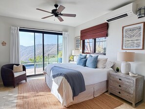 A bedroom with a large bed, a ceiling fan, a nightstand, a dresser, and a view of the outdoors. - Sapphire Peak 2br/2ba Private Pool, Panoramic Views, AC throughout, generator!!! (Coral Bay)