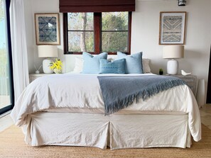 Un dormitorio con una cama grande, dos mesitas de noche, una ventana con vistas a árboles y dos lámparas de pared.