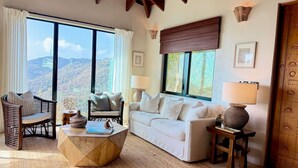 A cozy living room with a sofa, chairs, a coffee table, and a view of a mountainous landscape through large windows.