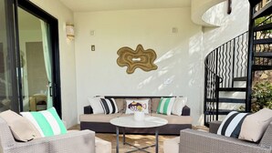 A furnished outdoor seating area with a sofa and two chairs, a round table, and a decorative wall piece.