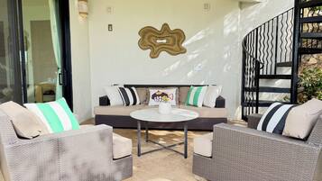 A furnished outdoor seating area with a sofa and two chairs, a round table, and a decorative wall piece.