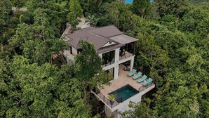 Una casa moderna de dos pisos rodeada de un bosque frondoso con una vista despejada al océano.