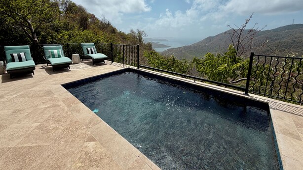 A swimming pool with two lounge chairs and a view of a mountainous landscape.