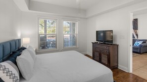 A bedroom with a bed, a TV on a wooden cabinet, and two windows with blinds. - Pool, Fitness Center & Central Location, Blue Mountain Beach + Free Tickets! (Santa Rosa Beach)