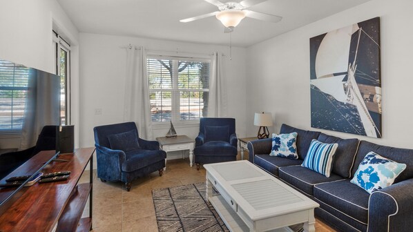 A living room with a sofa, two armchairs, a coffee table, a TV, and a ceiling fan. - Pool, Fitness Center & Central Location, Blue Mountain Beach + Free Tickets! (Santa Rosa Beach)
