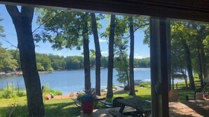 Eine Terrasse mit Bank und Blumentöpfen mit Blick auf einen See, Bäume und eine Rasenfläche.