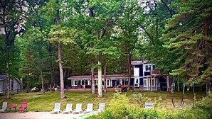Eine Hütte mit Veranda, umgeben von Bäumen und einem Teich.