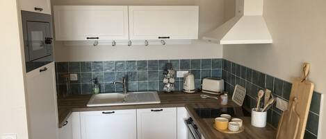 A compact kitchen with white cabinets, a sink, a stove, and a toaster.