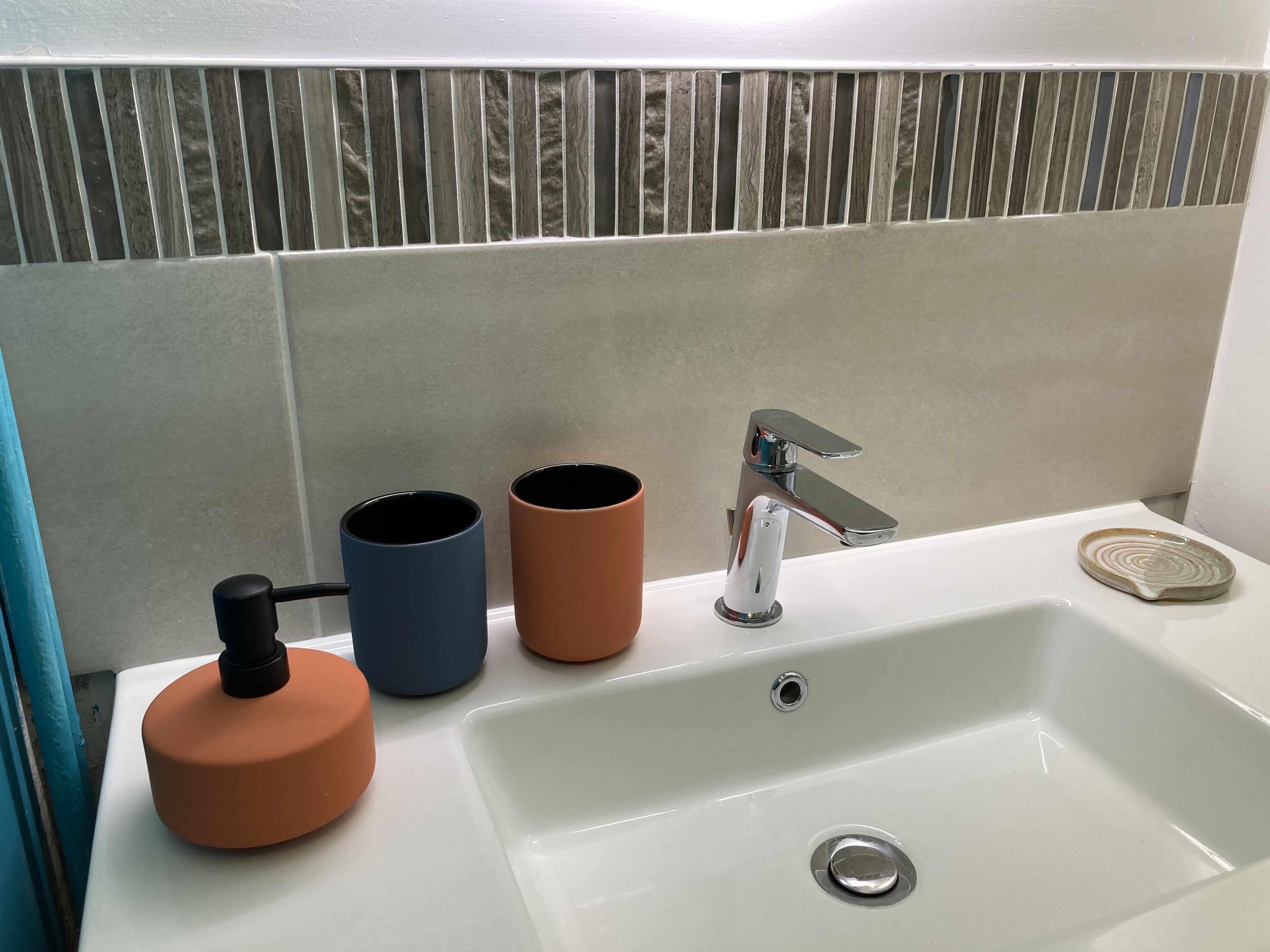 A bathroom sink with a chrome faucet, two ceramic cups, and a soap dish.