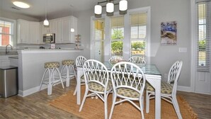 A kitchen with white cabinets, a central island with stools, and a dining table with chairs. - 5105 The Retreat - Barefoot Resort Rentals (North Myrtle Beach)