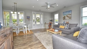 A spacious living room with a grey sofa, wooden coffee table, and a dining area with white chairs. - 5105 The Retreat - Barefoot Resort Rentals (North Myrtle Beach)