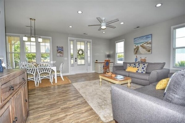 A spacious living room with a grey sofa, wooden coffee table, and a dining area with white chairs.