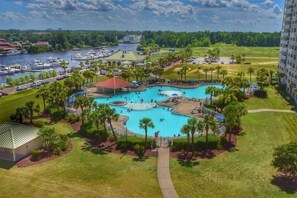 A resort with a large central pool, a marina with boats, and a lush green landscape.