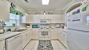 A kitchen with white cabinets, a microwave, stove, and a refrigerator. There is a window with blinds, a sink, and a rug on the floor. - 533 Wedgewood - Barefoot Resort Rentals (North Myrtle Beach)