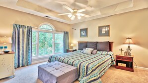 A bedroom with a large bed, a ceiling fan, a window with curtains, a nightstand with a lamp, and a small wooden cabinet. - 533 Wedgewood - Barefoot Resort Rentals (North Myrtle Beach)