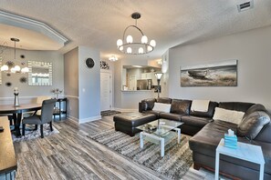 A modern living room with a sectional sofa, a glass coffee table, and a dining area with a wooden table and chairs. - 427 Harbour Cove - Barefoot Resort Rentals (North Myrtle Beach)