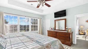 A bedroom with a large bed, a dresser, a TV mounted on the wall, and a ceiling fan.