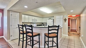 Une cuisine moderne avec des meubles blancs, un îlot central doté de tabourets de bar et un plafond pourvu d’un éclairage encastré.