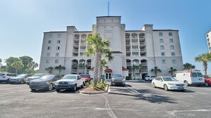 Un hôtel à plusieurs étages, doté d’une entrée principale, de nombreux balcons et d’un parking où sont stationnées plusieurs voitures.