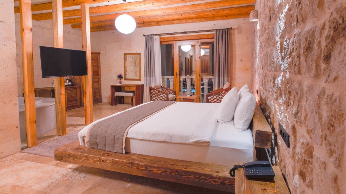 A bedroom with a wooden bed, a desk, a chair, a television, and a telephone.