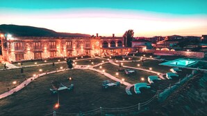 Une cour avec une piscine, des espaces de détente en plein air et un bâtiment en pierre doté de nombreuses fenêtres et d’arcades.